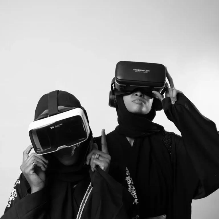 A black and white photo of two individuals wearing hijabs and VR headsets, gesturing with their hands.